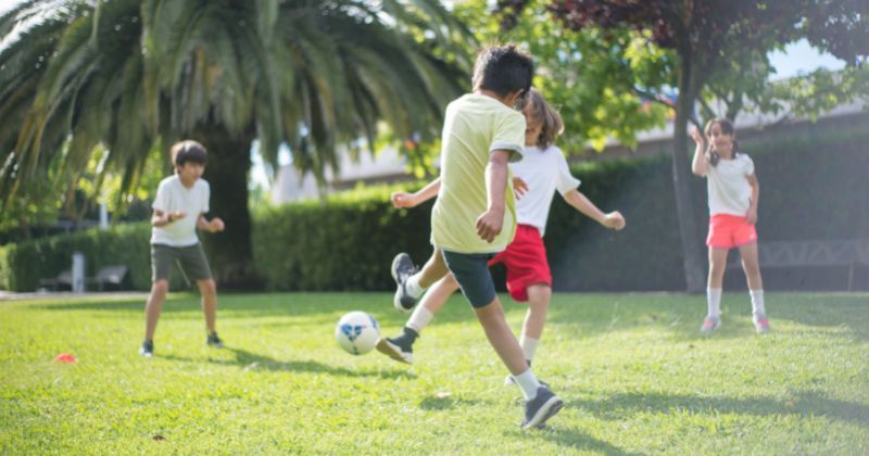 child kicking football at other children