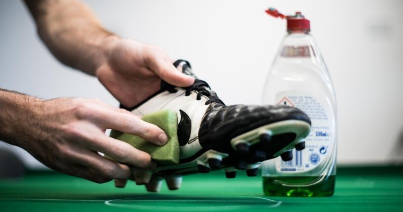 dirty football boots being cleaned with a sponge