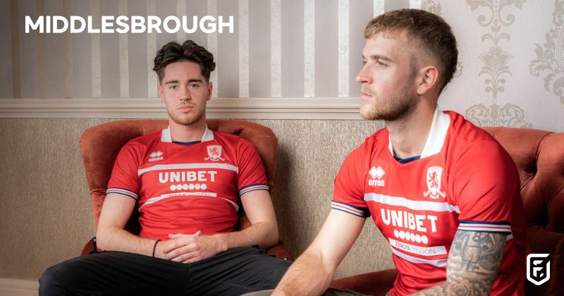 two players sat on sofas wearing middlesbrough 2023-24 home shirts in red and white